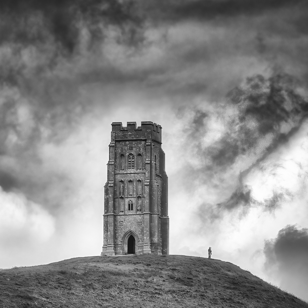 Een eenzame bezoeker staat op de rand van de heuvel naast Glastonbury Tor, Somerset, Verenigd Koninkrijk.